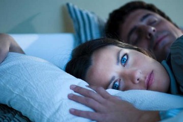 Femme allongée insomniaque à côté de son mari
